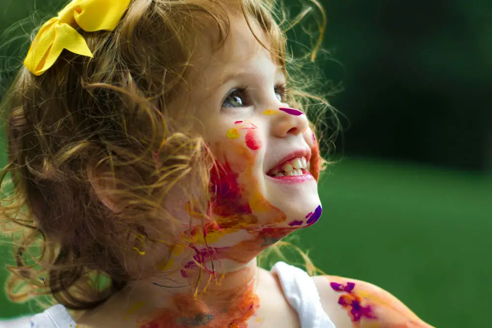 smiling little girl with colorful paint on her face and yellow bow in her har