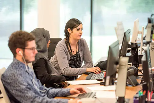 Two women and one man sitting at a desk with computers